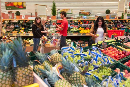 Ein Mitarbeiter im CAP-Markt berät zwei Kundinnen in der Obst und Gemüseabteilung.