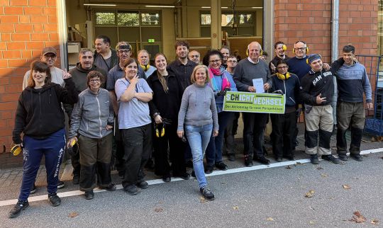 Eine Gruppe Teilnehmer posiert gemeinsam vor einer Werkshalle für ein Foto