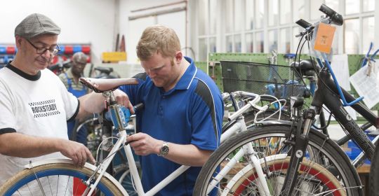 Eine Reparatur eines Rennrades durch zwei Personen in einer Werkstatt.