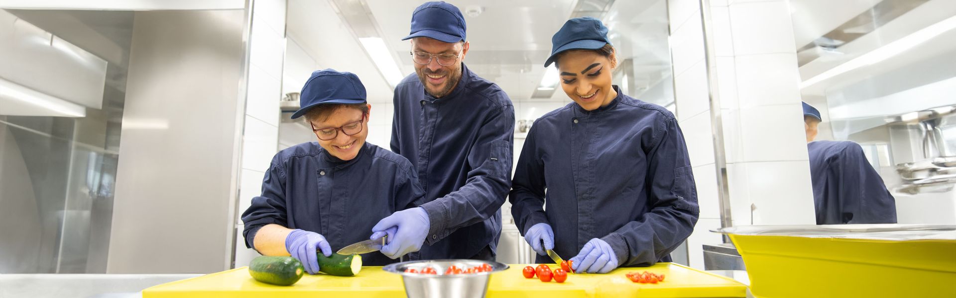 Drei Fachangestellte in der Gastronomie schneiden zusammen Gemüse