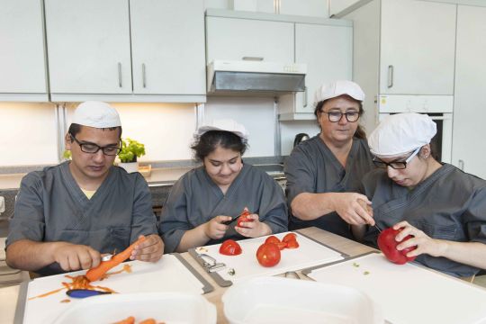 Vier Mitarbeitende des Lehrcafés bei Hausarbeiten. Sie schälen Karotten, Tomaten und Paprikas.